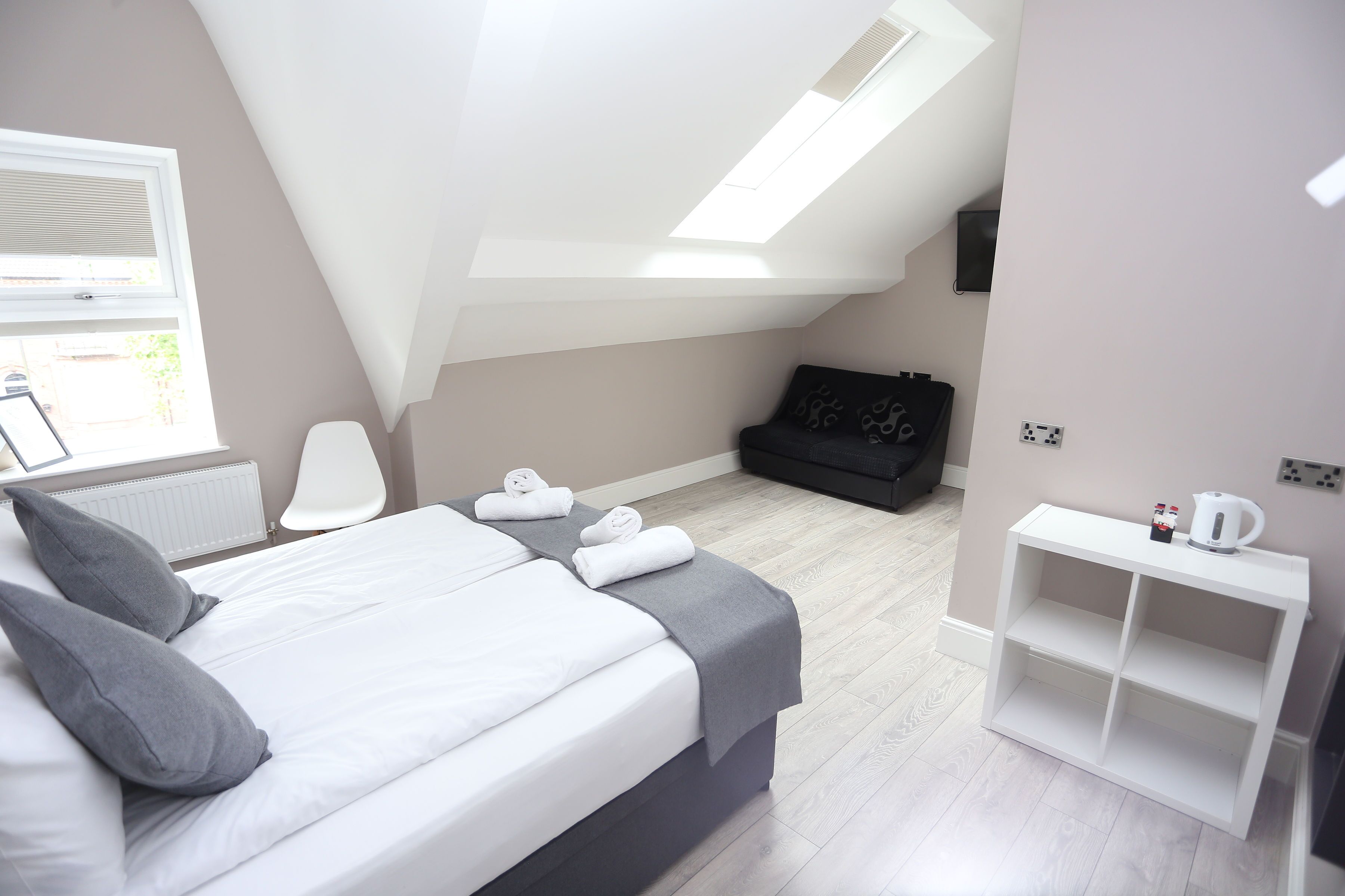A modern bedroom with a bed, a desk, a chair, and a small black sofa.