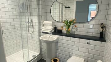 A modern bathroom with white subway tiles, a glass shower enclosure, a white sink, a toilet, and a mirror above the sink.