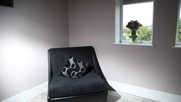 Une pièce d’angle avec une chaise de couleur sombre, une fenêtre donnant sur des arbres et un vase de fleurs posé sur le rebord de la fenêtre.