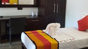 A hotel room with a bed, a desk, a wardrobe, and a small table with a chair. - Ayubowan Resorts (Avudangawa)