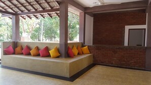 A covered seating area with a bench and colorful cushions, a brick wall, and a window overlooking greenery. - Ayubowan Resorts (Avudangawa)