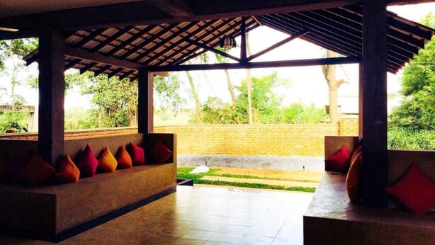 An open-air covered seating area with a view of a garden. - Ayubowan Resorts (Avudangawa)