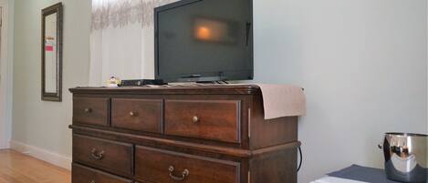 Une pièce avec une commode en bois, un téléviseur posé dessus et un appareil électroménager blanc sur la droite.