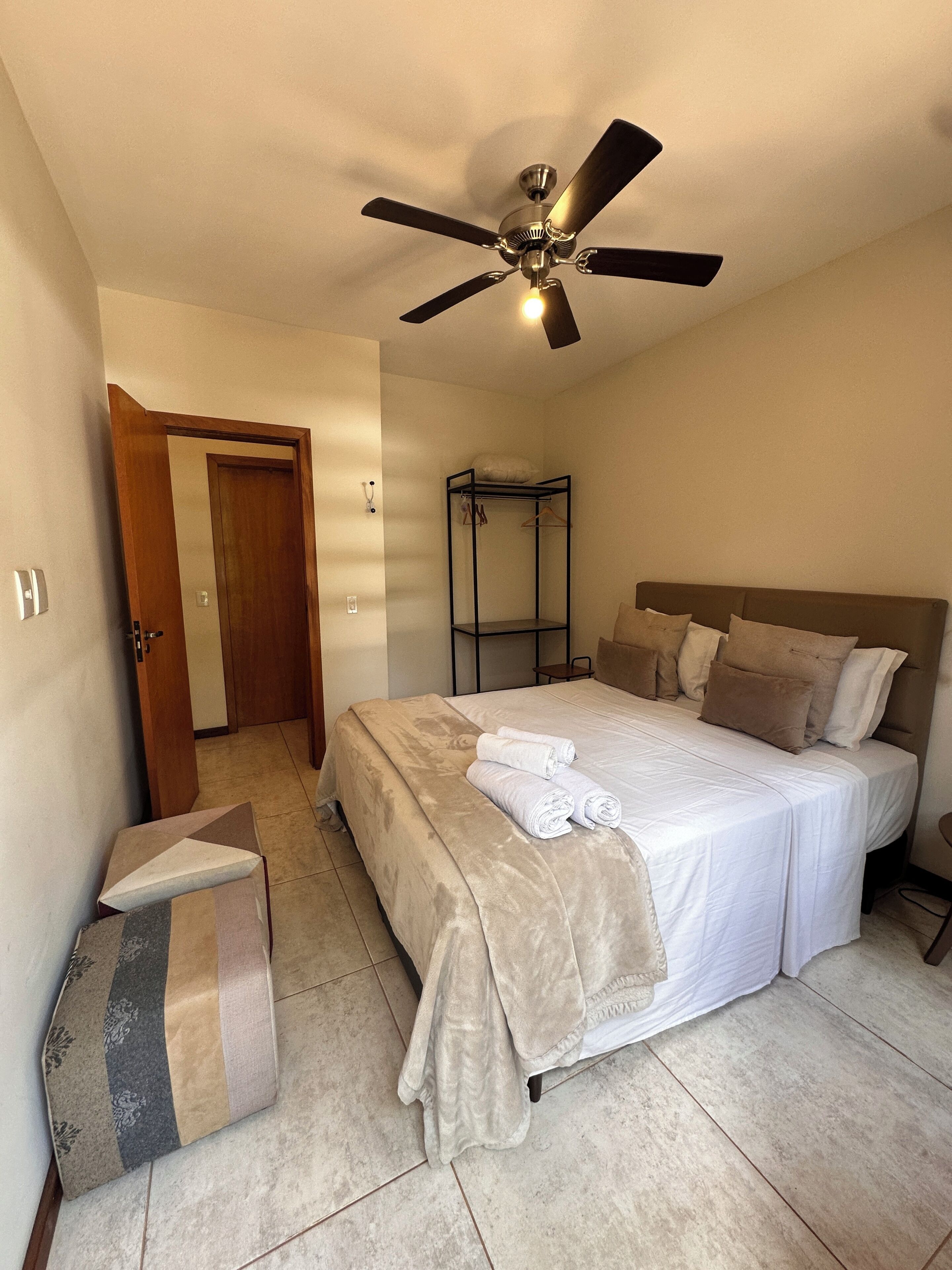 Quarto com cama, ventoinha no teto, guarda-roupa e uma porta.