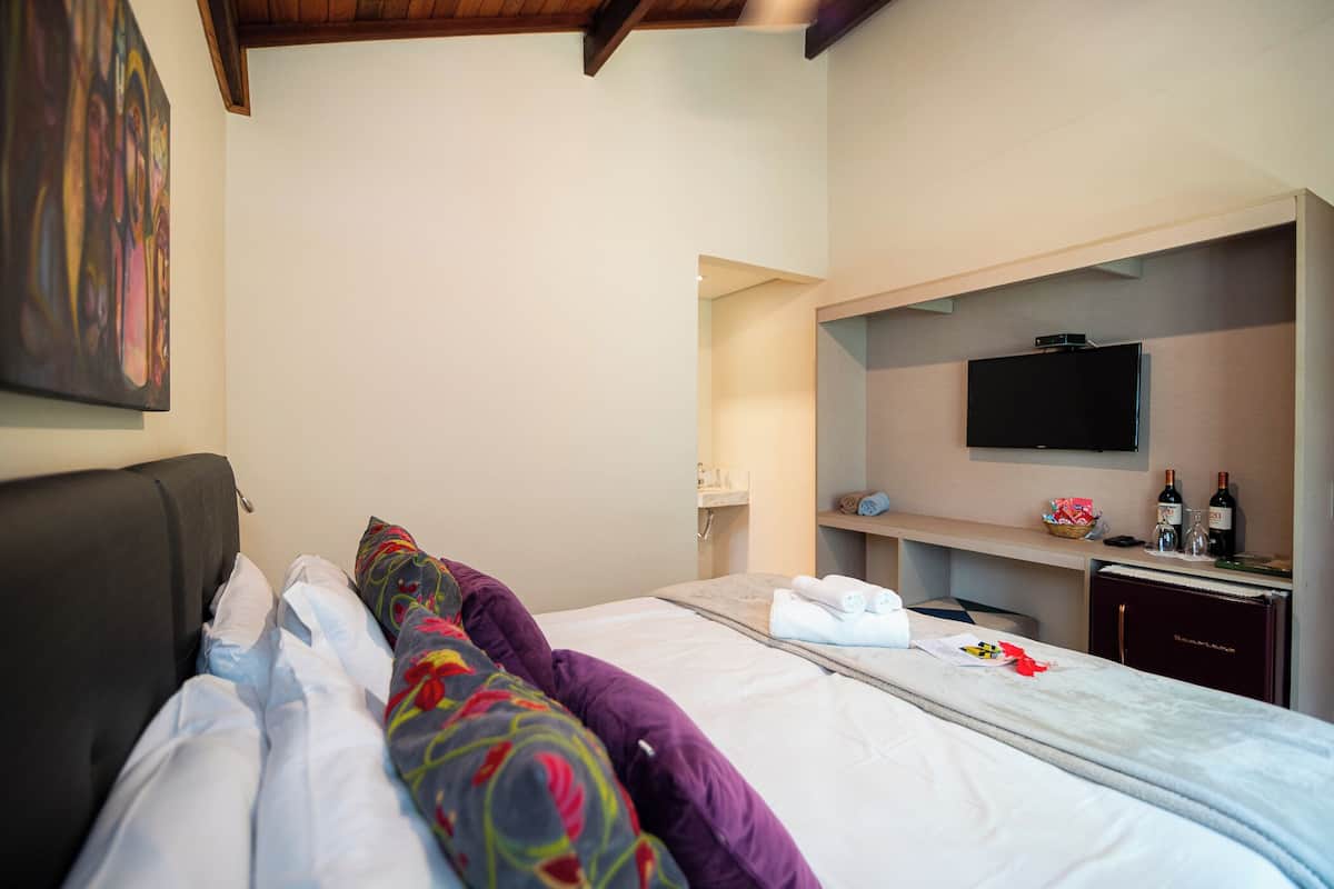 A hotel room with a bed, a television, a minibar, and a painting on the wall.