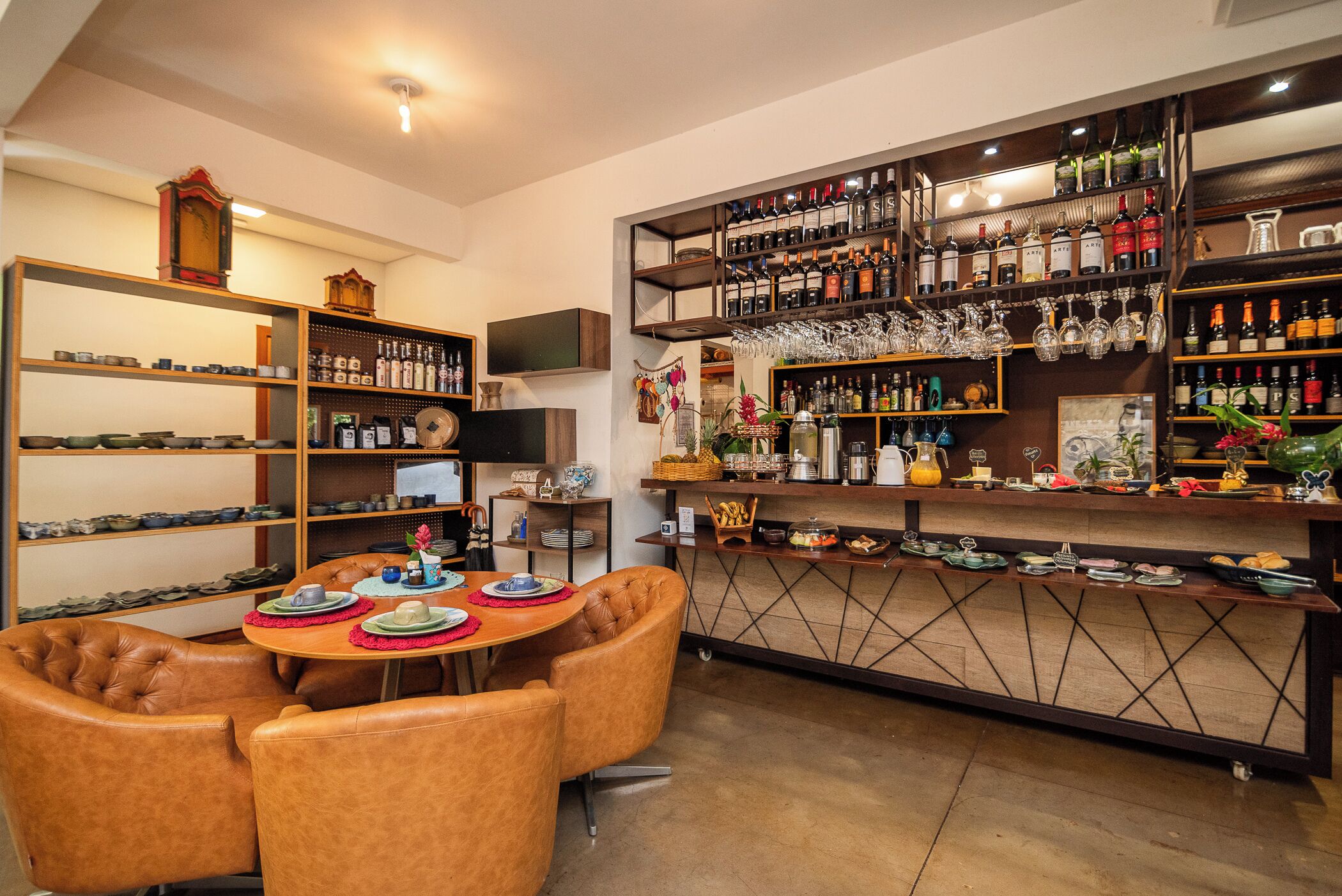 A bar area with shelves of bottles and glasses, a dining table with chairs, and a clock on the wall.