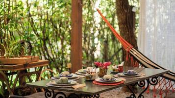 Un área de comedor al aire libre con mesas dispuestas para una comida, rodeada de abundante vegetación.