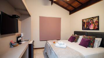 A hotel room with a bed, a flat-screen TV, a painting on the wall, and a window with a blind.