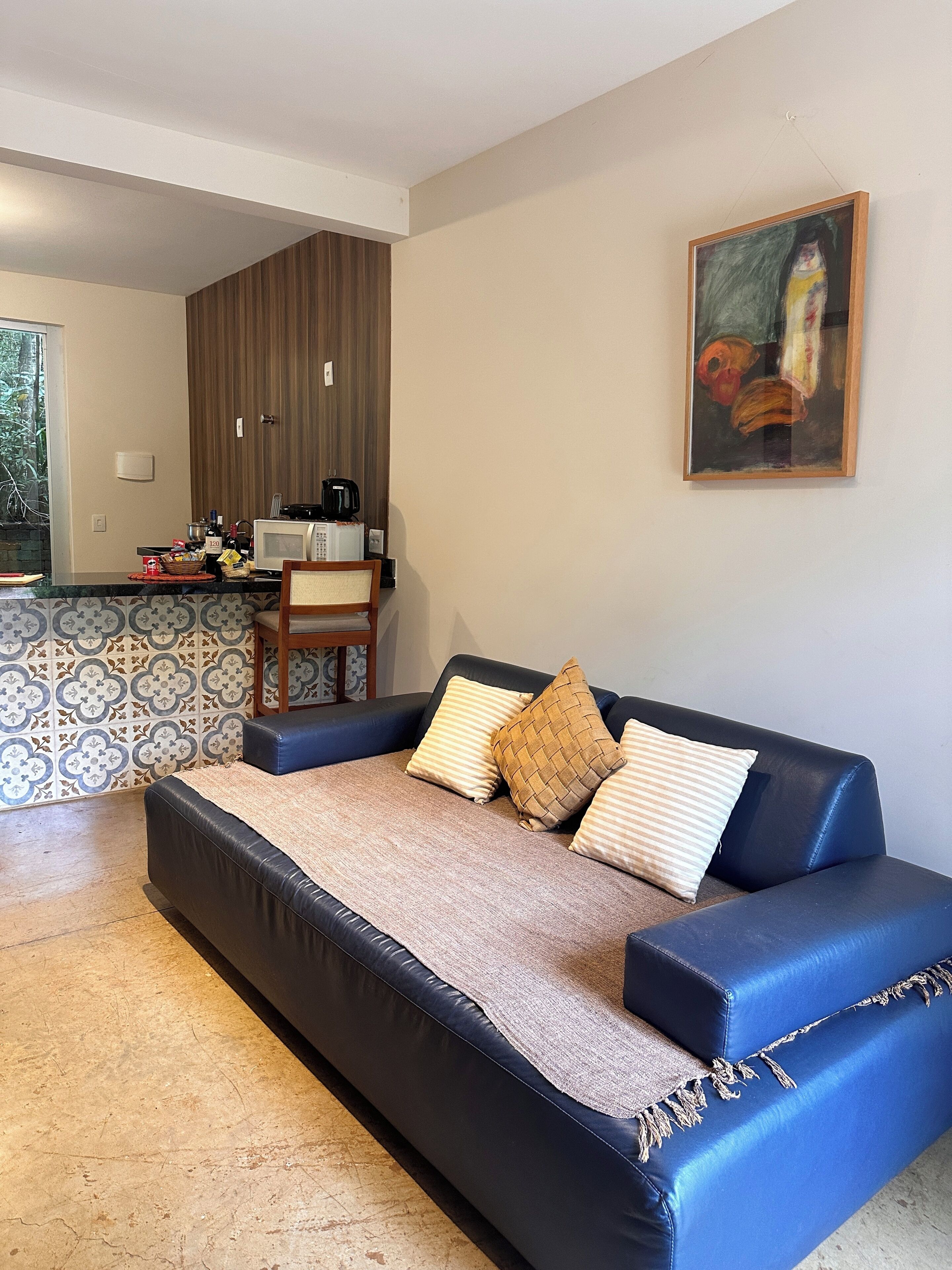A modern living room with a sofa, a kitchen area, and a painting on the wall.