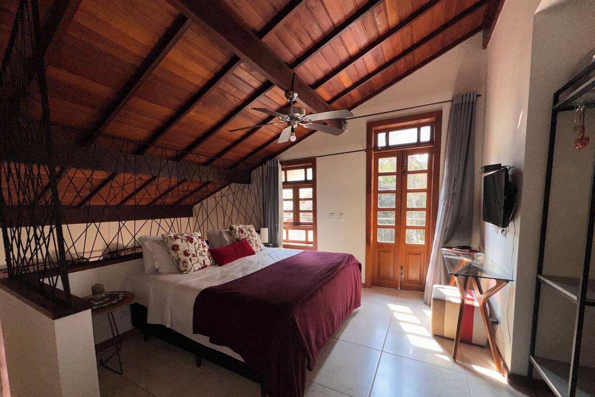 A bedroom with a bed, a ceiling fan, a TV, and a door leading to another room.