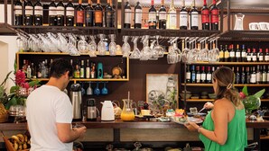 A bar area with shelves of wine bottles and glasses, a coffee machine, and a counter with food and drinks.