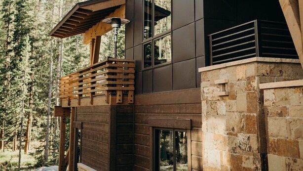 A modern wooden cabin with large windows and a stone foundation, surrounded by a forest. - River's Edge 4 Bedroom Home by RedAwning (Breckenridge)