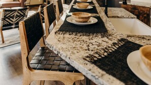 A modern kitchen with a stone backsplash, wooden chairs, a long dining table, and a hanging light fixture. - River's Edge 4 Bedroom Home by RedAwning (Breckenridge)
