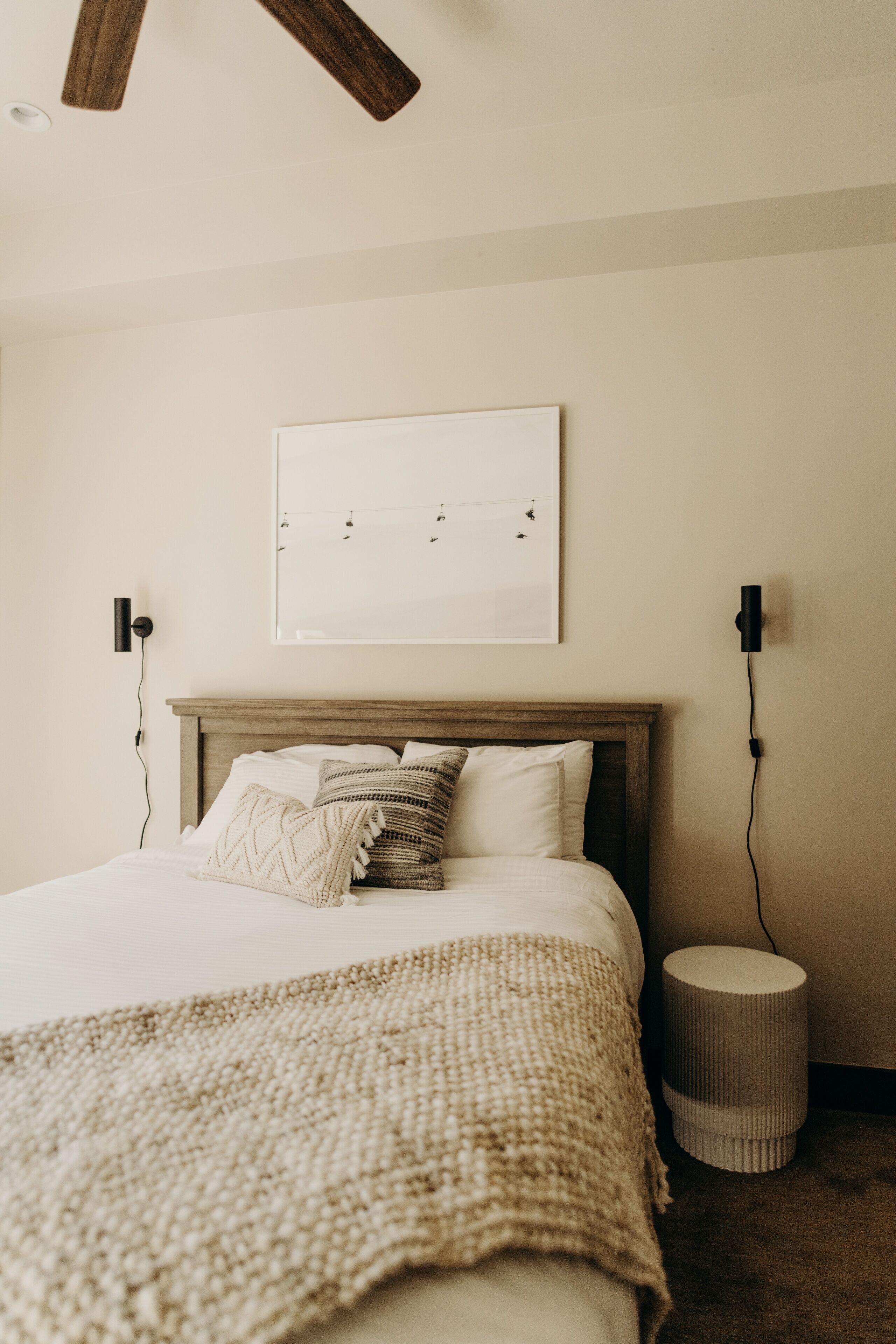 Un dormitorio con cabecera de madera, una cama grande con ropa blanca, una mesita redonda y dos altavoces montados en la pared.