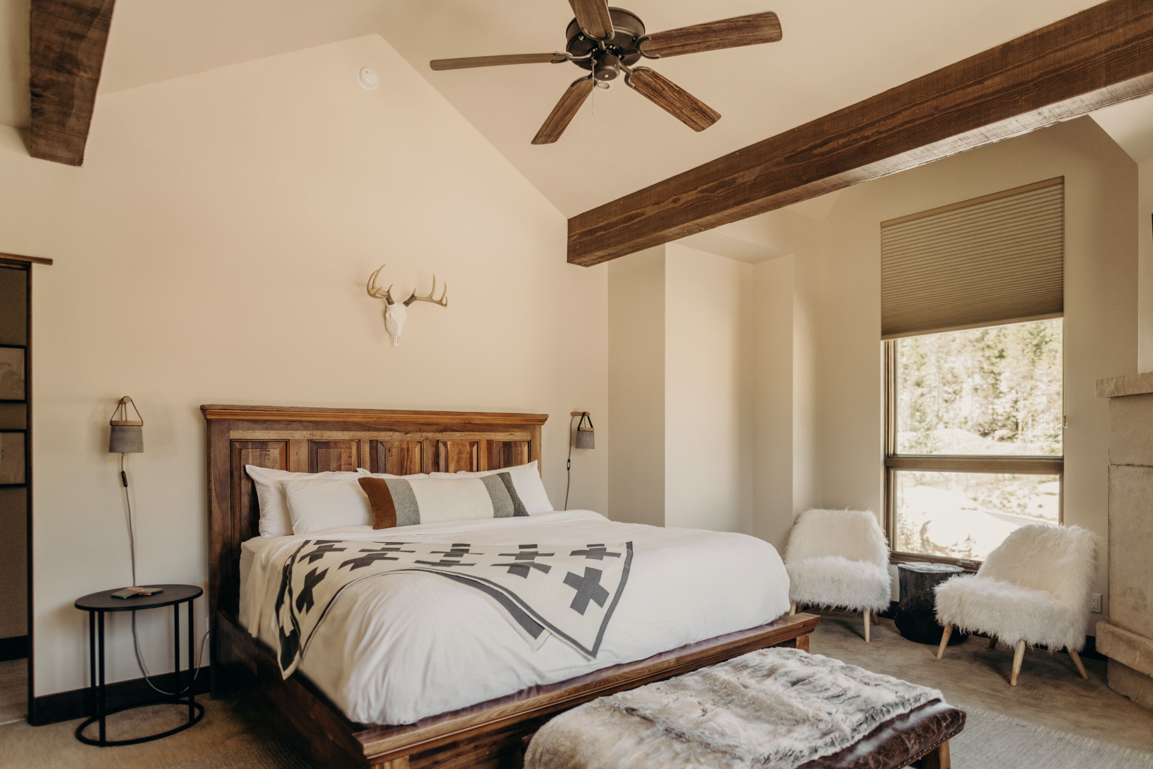 A bedroom with a wooden bed, a ceiling fan, a window with blinds, and a wall-mounted deer head decoration.