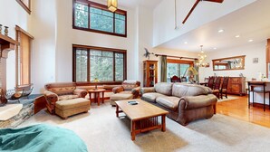 A spacious living room with a large sectional sofa, a coffee table, and a fireplace. There are multiple windows providing natural light and a view of the outdoors. - Timbers 5 Large Luxury Home with Two Master Suites, Perfect for Families by RedAwning (Mammoth Lakes)
