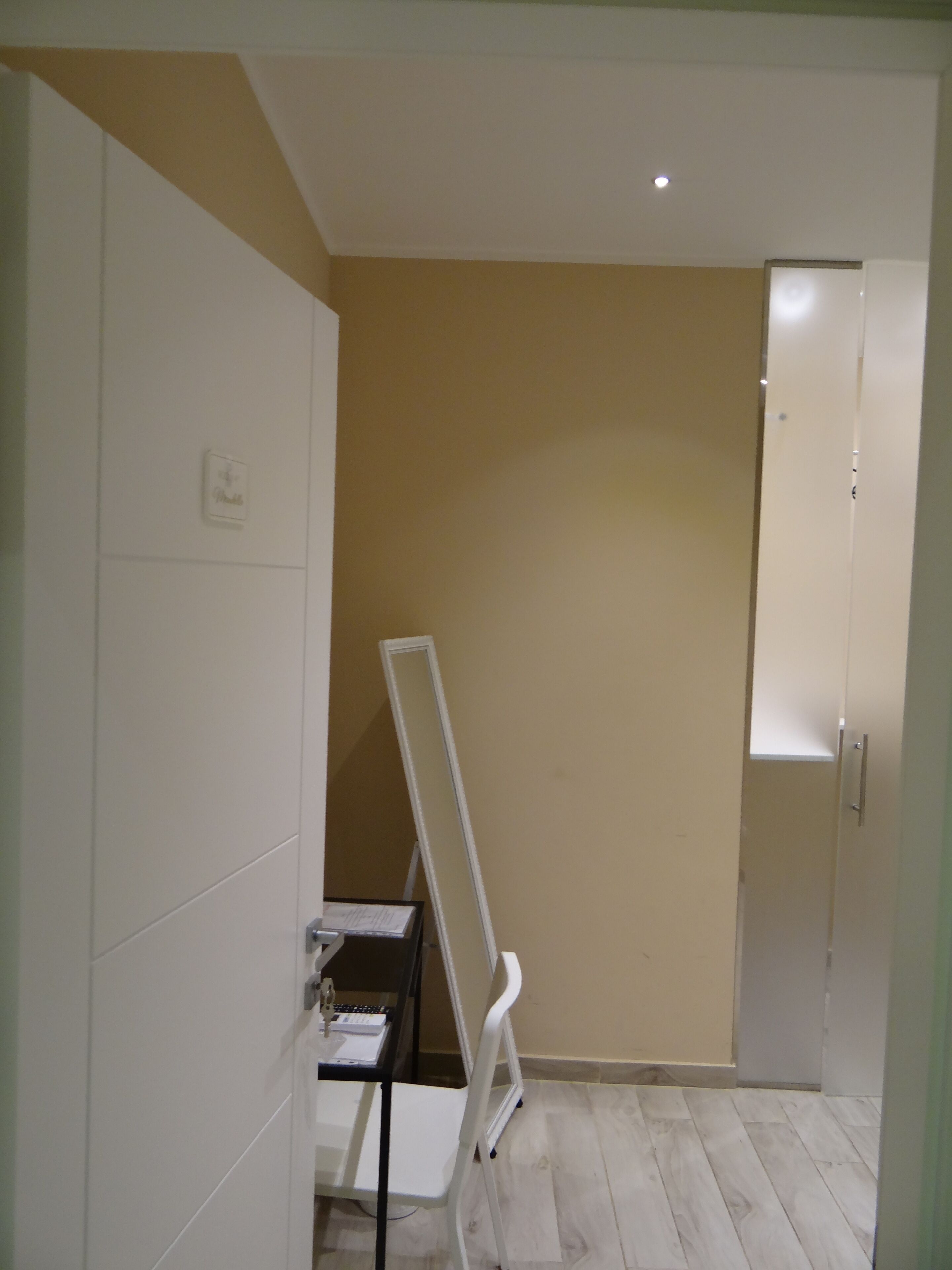 A room with a white wardrobe, a white desk with a chair, and a white folding chair.