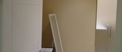 A room with a white wardrobe, a white desk with a chair, and a white folding chair.