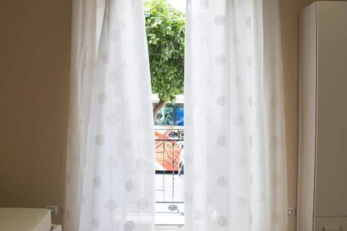 Una habitación con cama, armario y vistas a través de una ventana con cortinas.