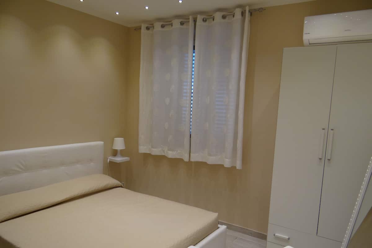 Un dormitorio con una cama, una mesita de noche, una lámpara, un armario y una ventana con cortinas.