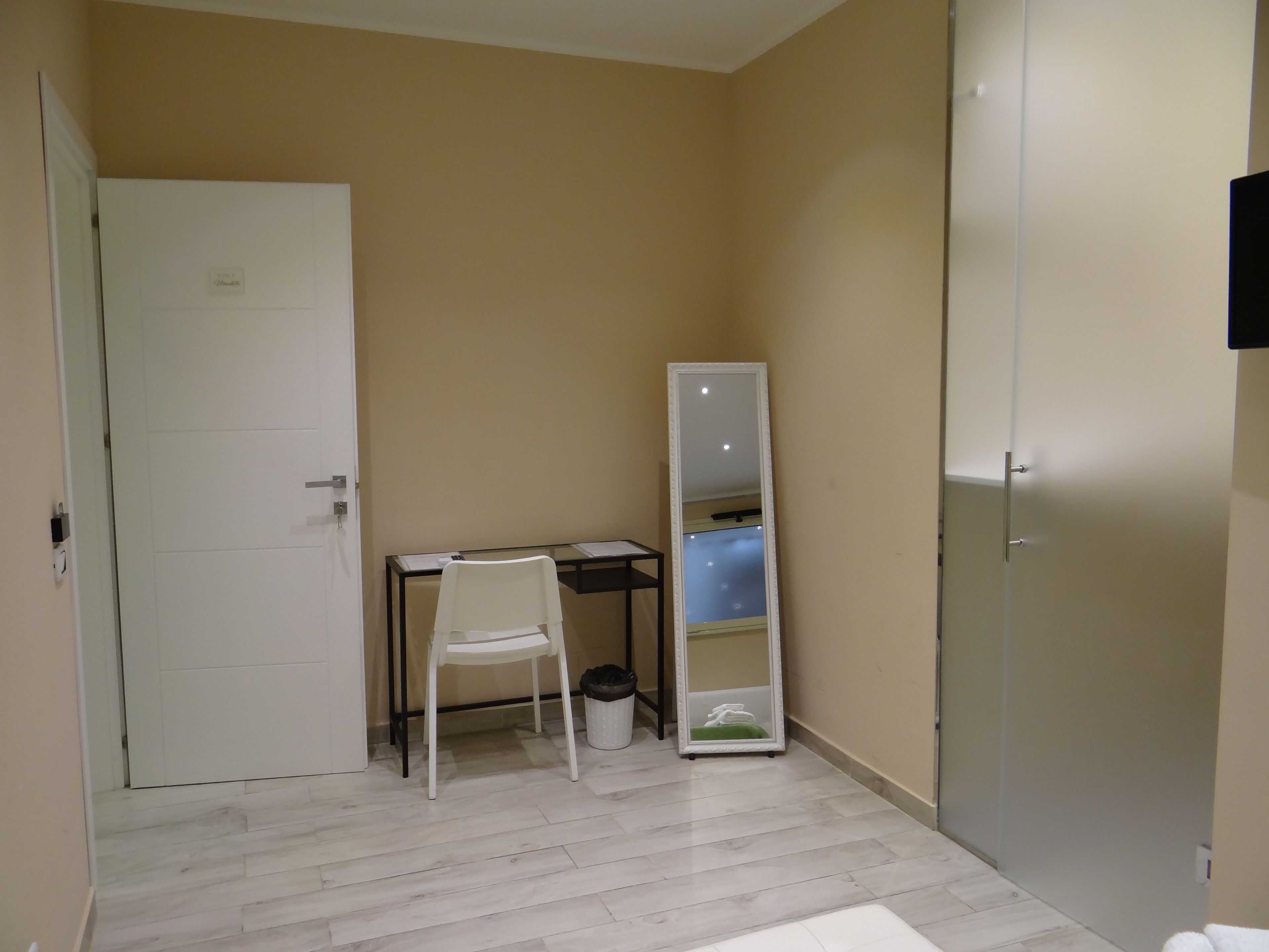 Une petite pièce avec une porte blanche, un bureau avec une chaise, un miroir et une poubelle.