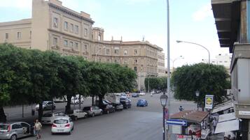 A street view with parked cars, a pedestrian, and a building with classical architecture.