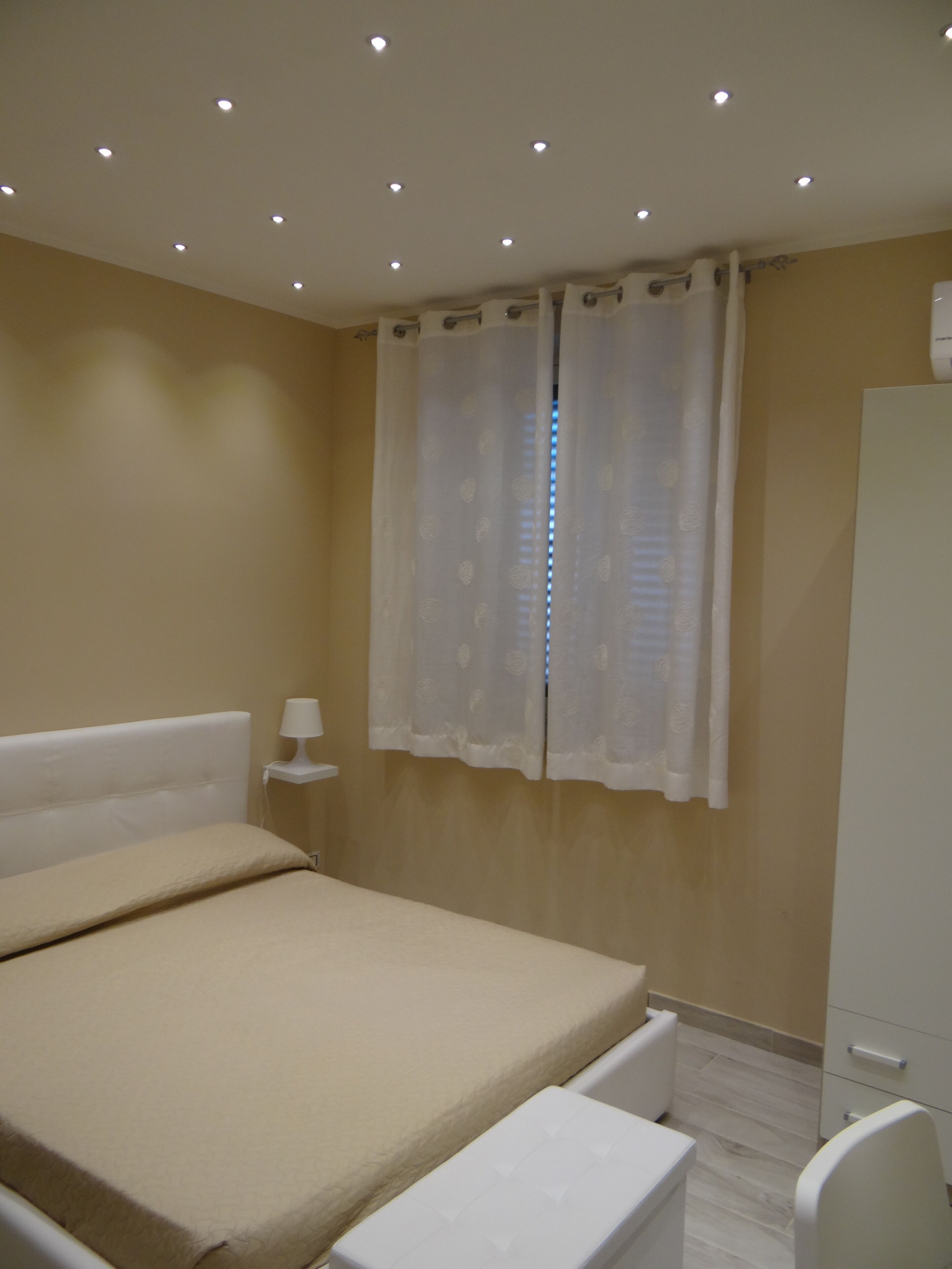 A bedroom with a bed, a nightstand, a wardrobe, and a window with curtains.
