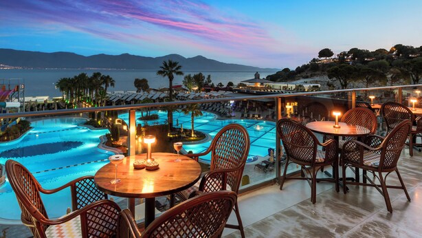 A rooftop pool area with lounge chairs and tables, overlooking a scenic view of the sea and mountains. - Liberty Kuşadası - All inclusive (Kusadasi)