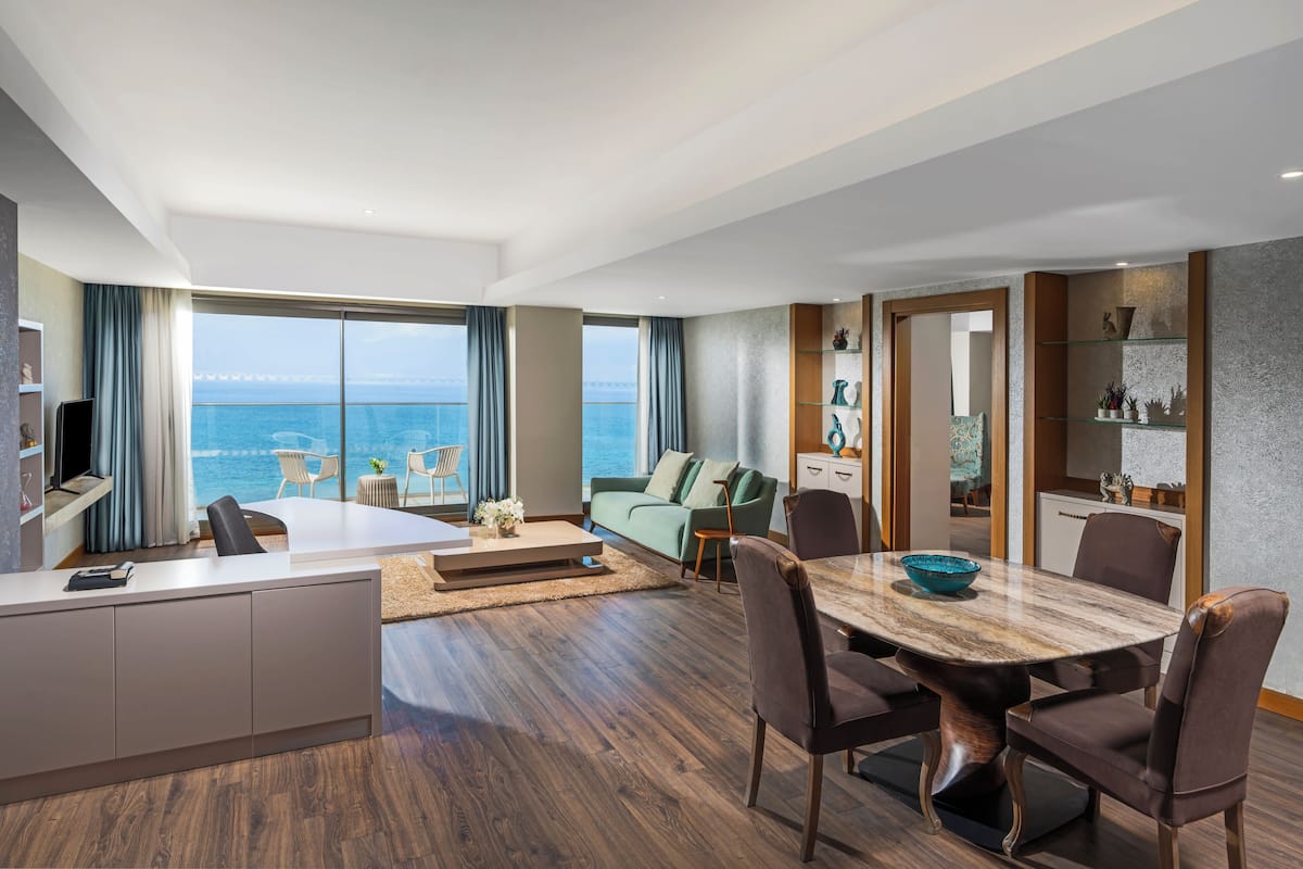 Ein modernes Wohnzimmer mit einem großen Esstisch, Sitzgelegenheiten und Meerblick.