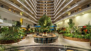 A modern hotel atrium with a central bar area, multiple floors, and abundant indoor greenery. - Liberty Kuşadası - All inclusive (Kusadasi)