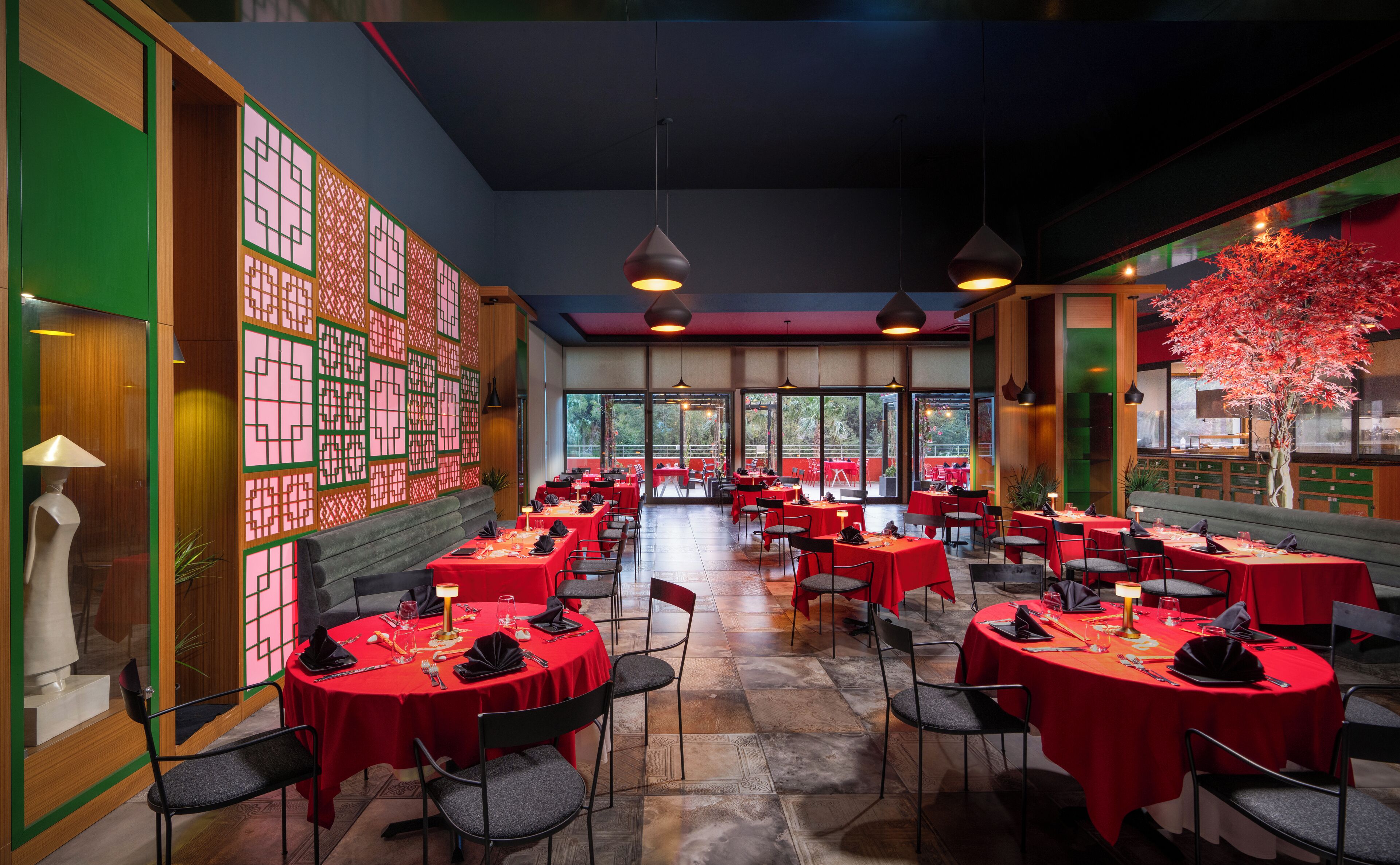 Ein Restaurant mit runden Tischen, die mit roten Tischdecken bedeckt sind, schwarzen Stühlen und Pendelleuchten.