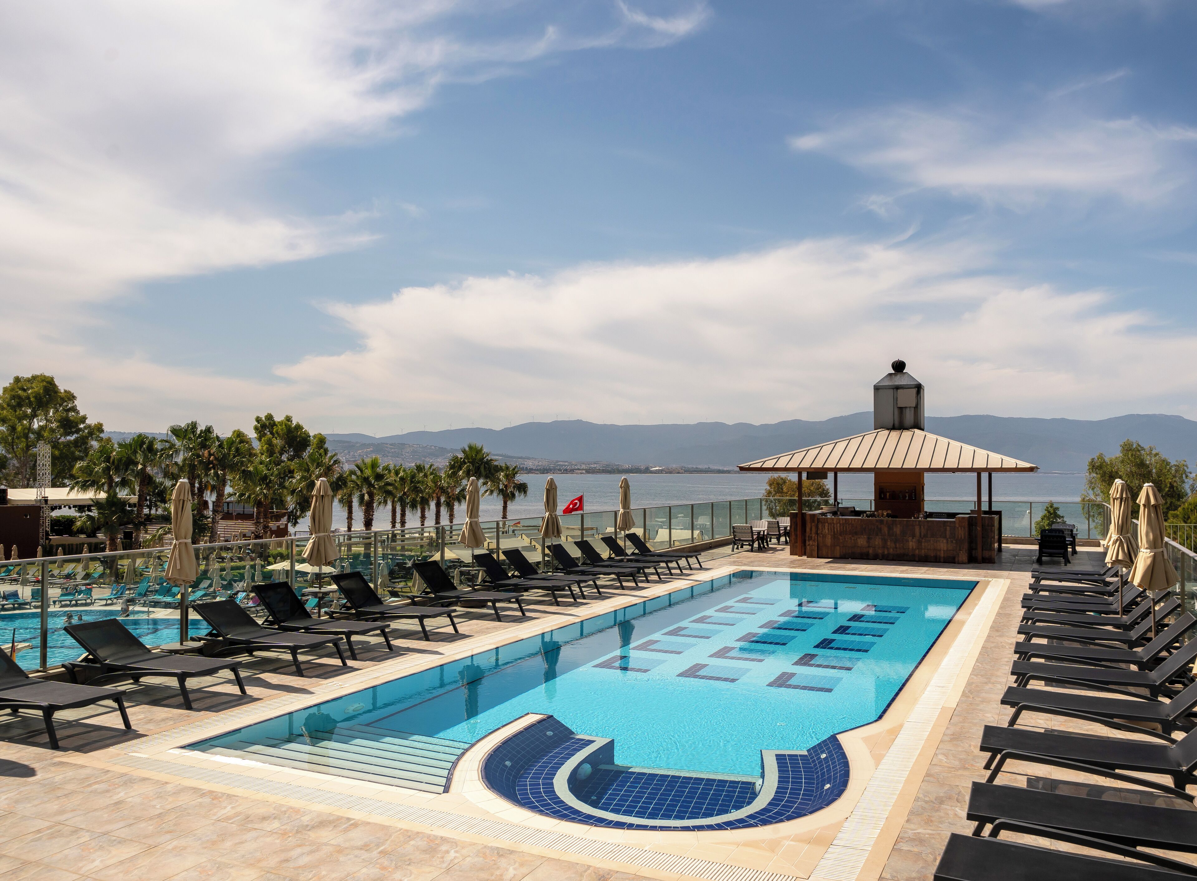 Ein Poolbereich mit Liegestühlen, einem Whirlpool und Blick auf das Meer und die Berge.