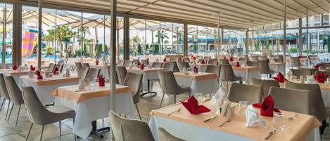 A spacious outdoor dining area with multiple tables and chairs, large windows, and a view of a water park.