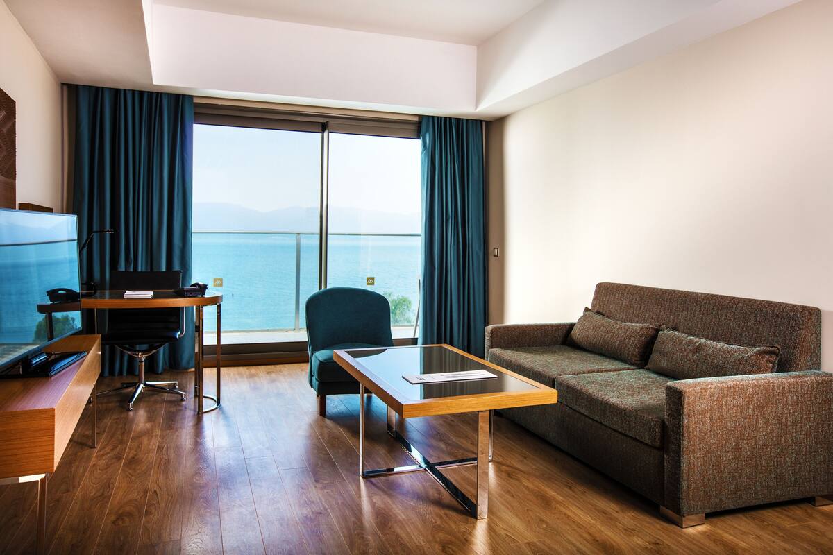 Ein modernes Hotelzimmer mit einem Holztisch, einer gemütlichen Couch und einem großen Fenster mit Blick aufs Meer.