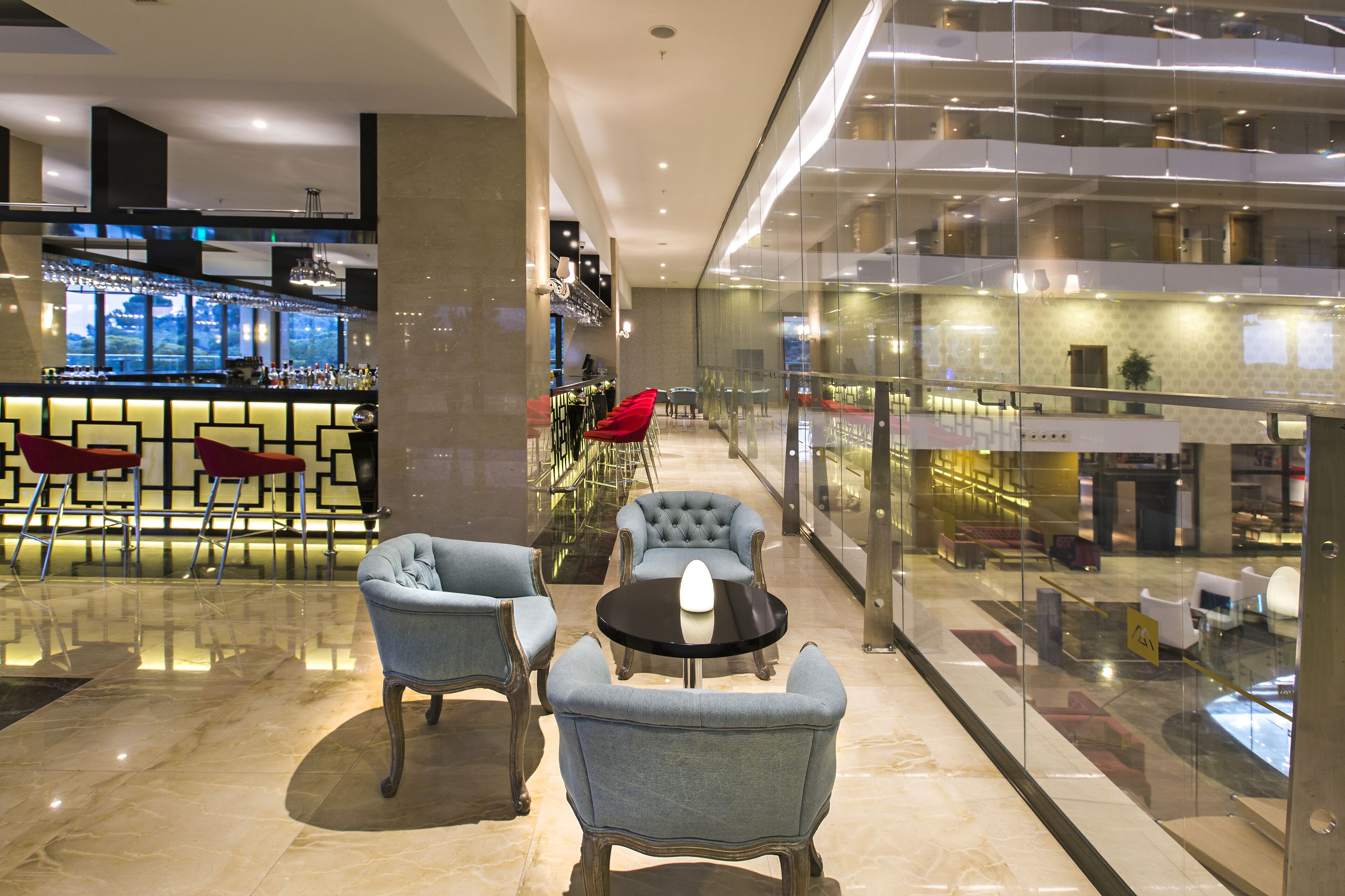 A modern lobby with a bar area, seating arrangements, and a glass-enclosed balcony.