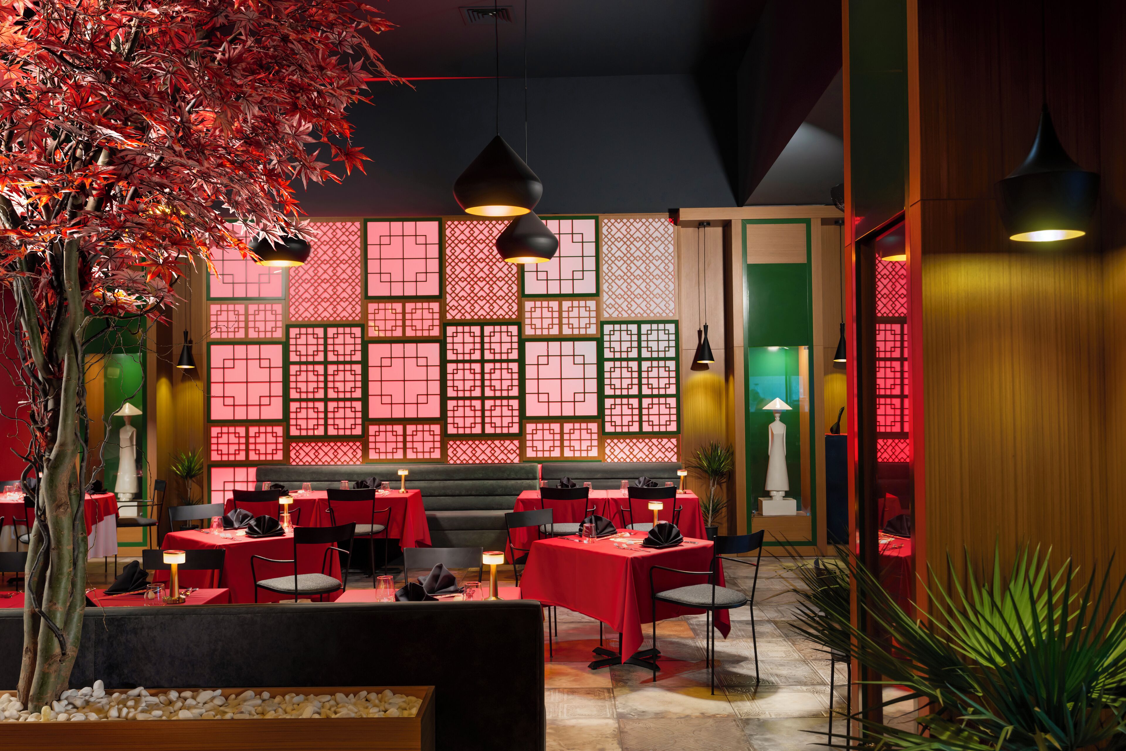 A restaurant with red tables and chairs, a decorative wall with geometric patterns, and hanging pendant lights.