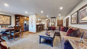 Un salón amplio con un sofá grande, una zona de comedor con muebles de madera y una cocina con refrigerador y armarios de madera.
