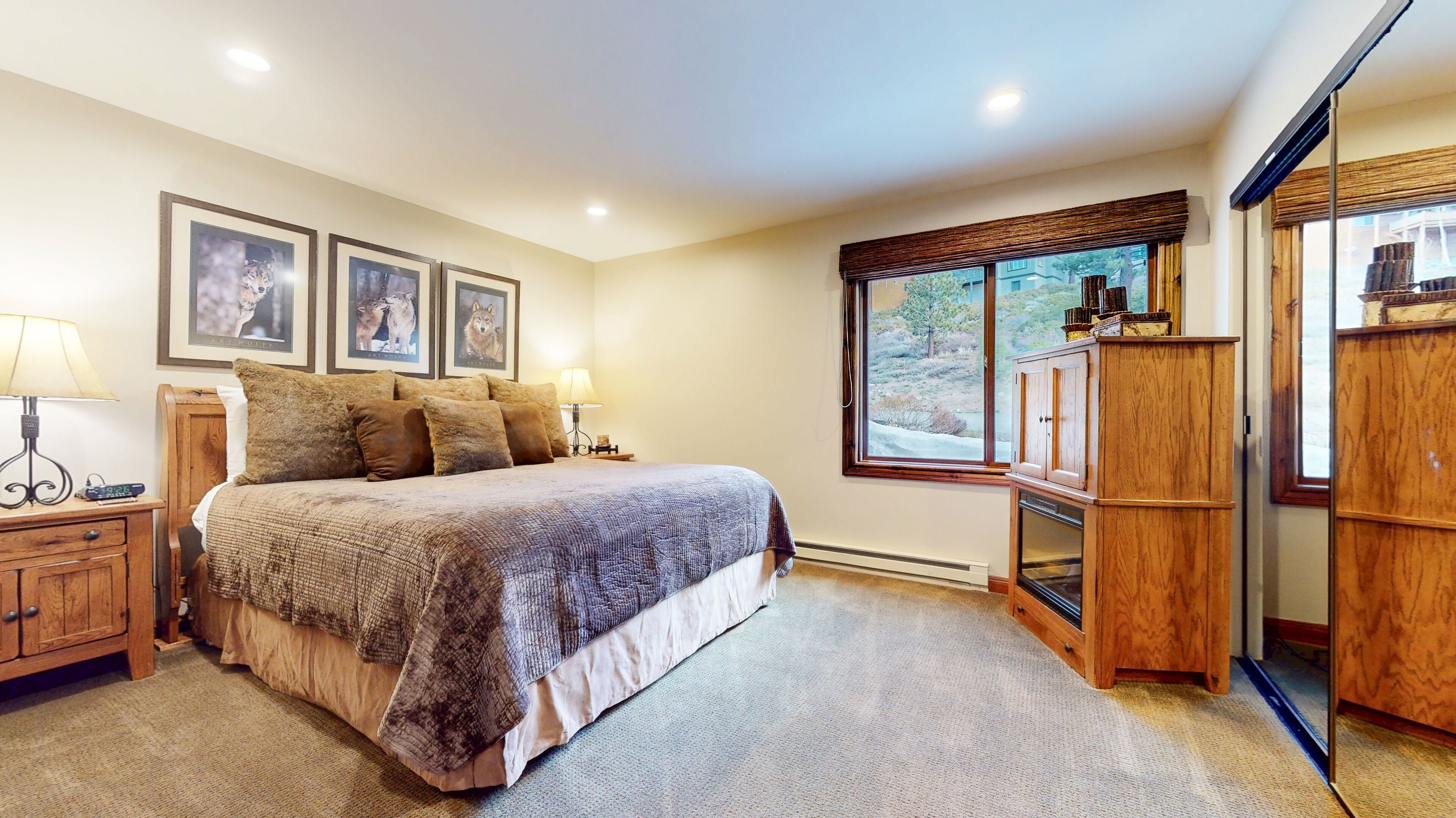 A bedroom with a large bed, wooden nightstands, a wardrobe, and framed pictures on the wall.