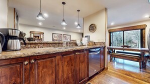 Una cocina con encimeras de granito, armarios de madera, cafetera e iluminación colgante.