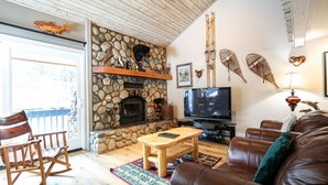 Uma sala de estar aconchegante com lareira de pedra, televisão, móveis de couro e arte decorativa nas paredes.