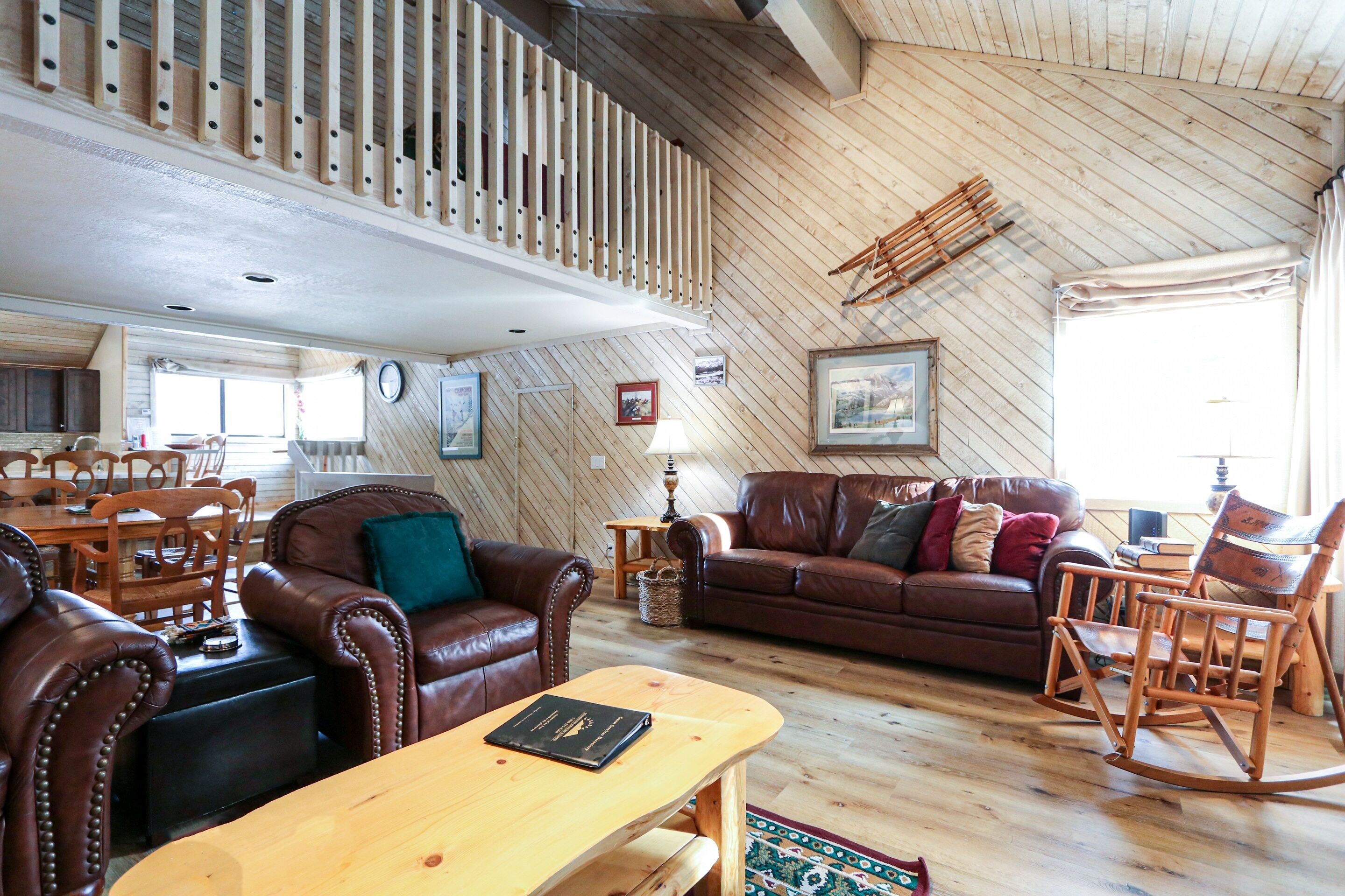 A spacious living room with leather sofas, a wooden coffee table, and a high wooden ceiling with exposed beams.