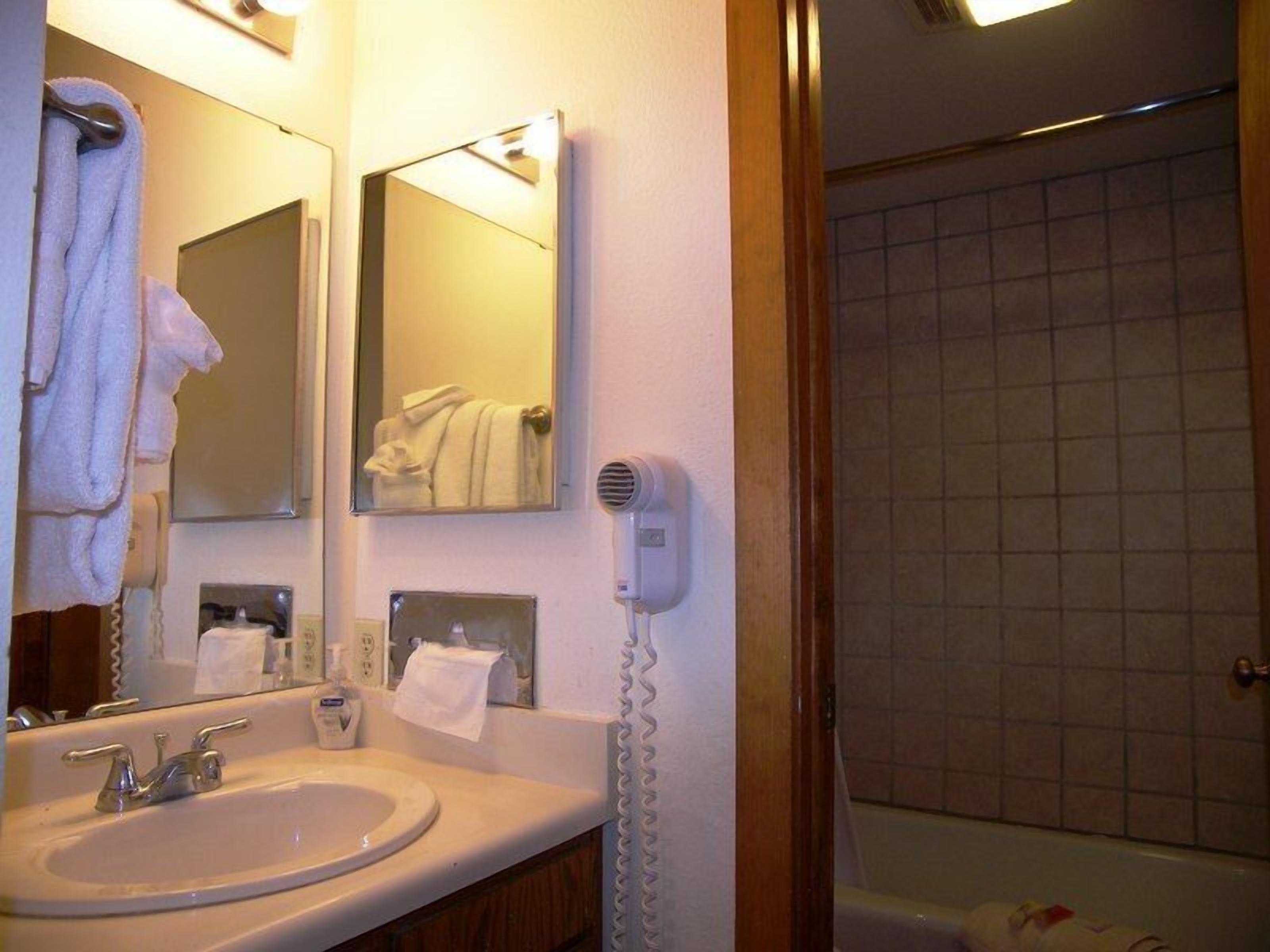 A bathroom with a sink, mirrors, a hairdryer, and a shower area.
