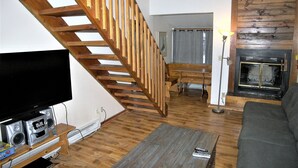 A living room with a wooden staircase, a fireplace, a television, and a sofa. - Fox Pine Lodge 4 Bed 4 Bath Condo (Copper Mountain)