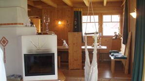 Un intérieur de chalet chaleureux avec une cheminée, des murs en bois, un coin repas et un fauteuil suspendu.