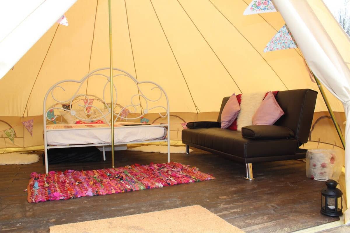 A tent with a bed and a sofa, a colorful rug, and a lantern.