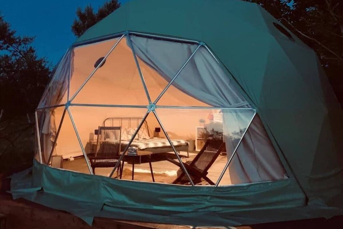 A geodesic dome tent with a bed and a chair inside.