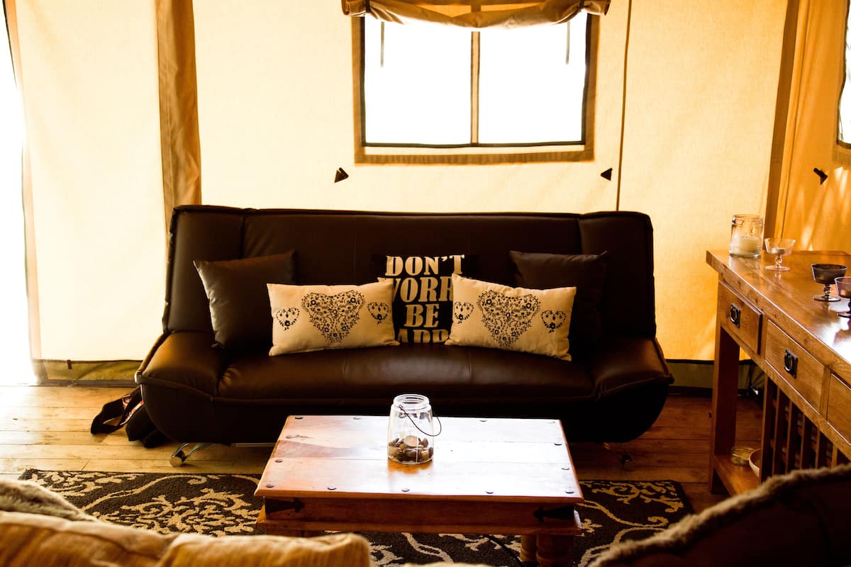 A cozy living room with a brown leather sofa, a wooden coffee table, and a window with curtains.