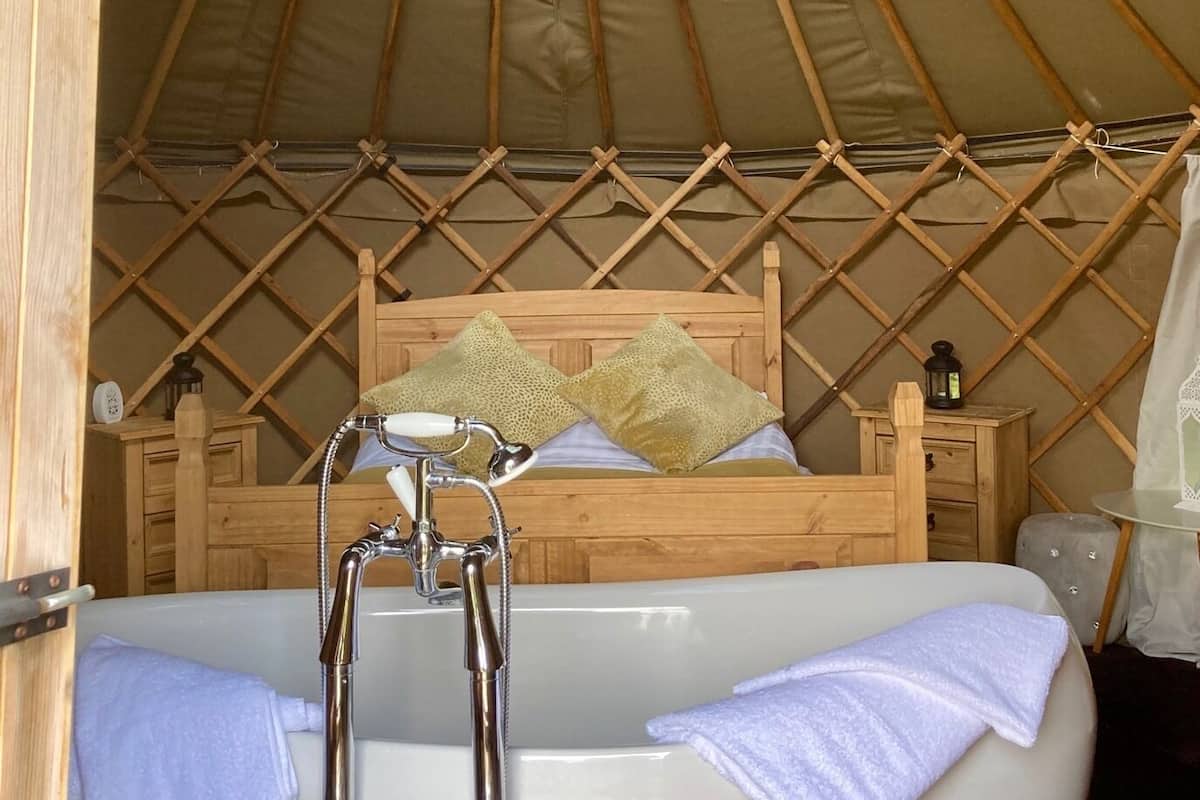 A yurt interior with a bed, a bathtub, and a wooden lattice ceiling.