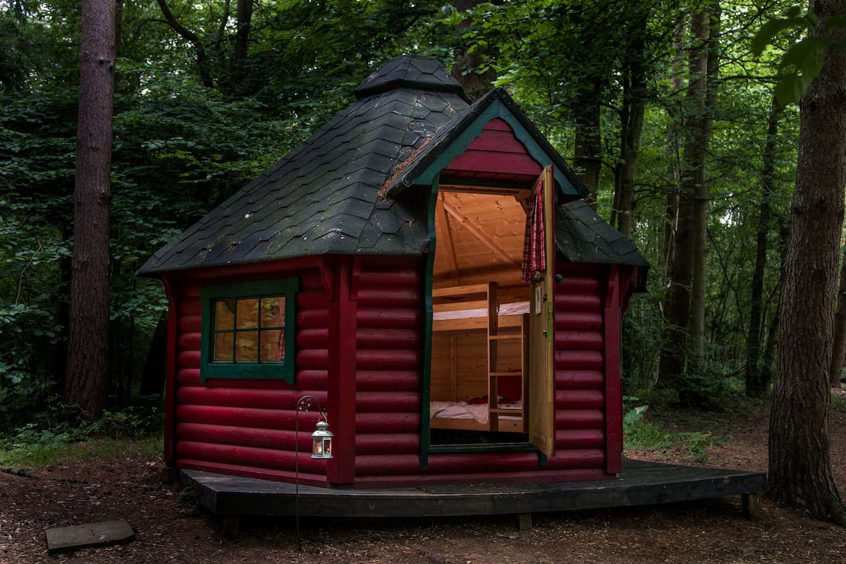 A small log cabin with a red exterior, a single window, and an open door leading inside.
