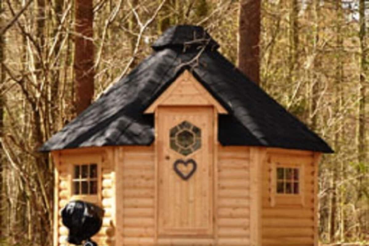 A small wooden cabin with a black roof, a heart-shaped decoration on the door, and a small black object on the ground.